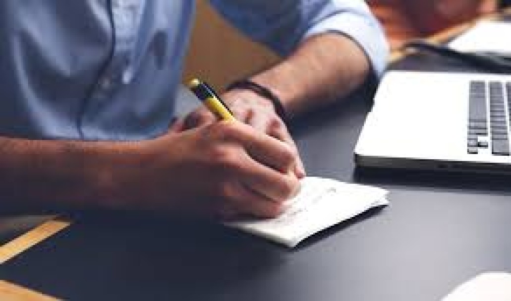 man writing on paper with yellow pen